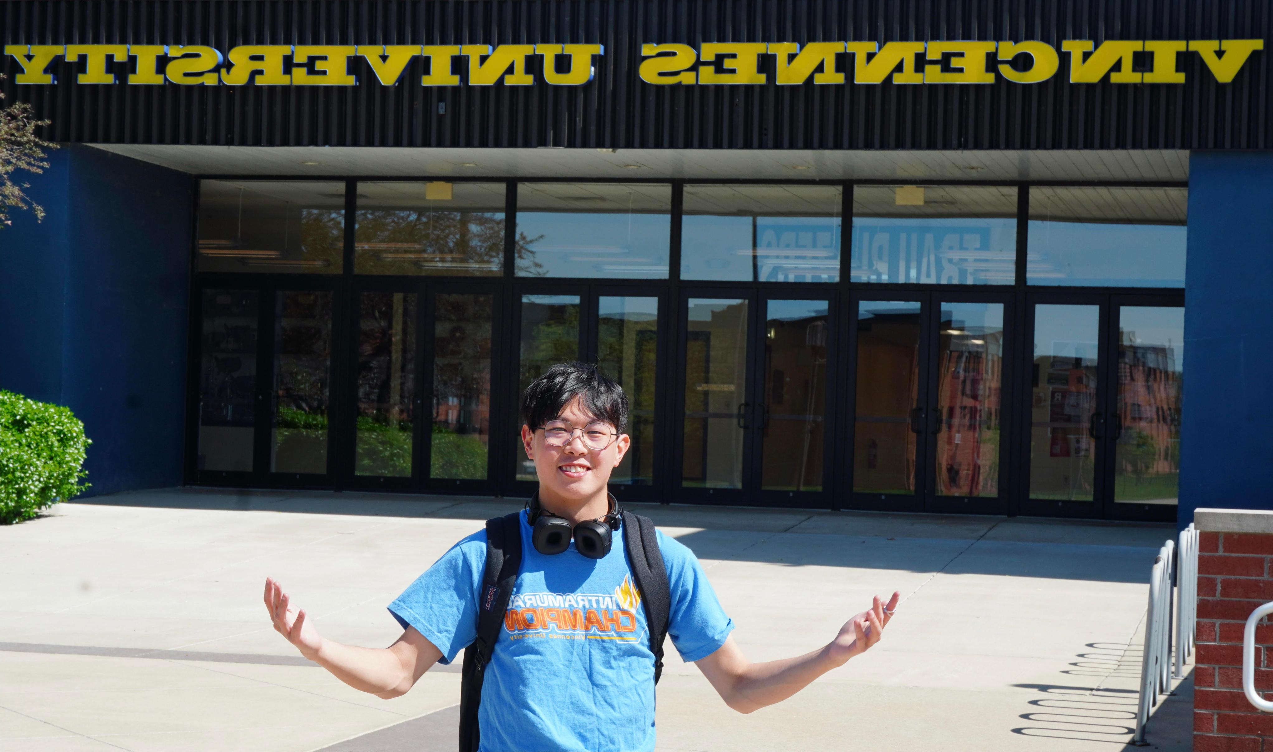 Samuel Lo stands with his arms extended in front of an entrance to the P.E. Complex. Vincennes University is displaced over the doors.er 